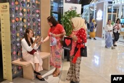 Seorang perempuan Indonesia (Tengah) mengajak pengunjung (L) sebuah mal untuk mengenakan pakaian nasional Indonesia "Kebaya" dalam kampanye "Selasa Berkebaya" di Jakarta, 30 Juli 2019. (ADEK BERRY/AFP)