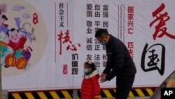 一名男子带着小女孩走过北京街头一面中国政府的宣传社会主义核心价值观的宣传墙。(2021年3月7日)