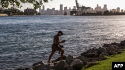 Seorang pria tampak berjalan di atas bebatuan di South Point Park di Miami Beach, Florida, di tengah gelombang panas yang melanda wilayah AS, pada 26 Juni 2023. (Foto: AFP/Giorgio Viera)