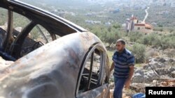 资料照片:2023年12月3日,一名巴勒斯坦男子在以色列占领的约旦河西岸萨尔菲特附近检查一辆在以色列定居者突袭中被烧毁的汽车。(路透社照片)