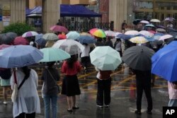 2024年6月7日中国高考第一天,北京考生进入考场后,家长和老师打着伞等候在考场外。