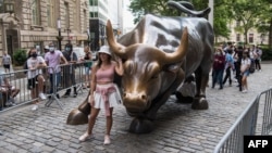 资料照:游客与纽约曼哈顿的华尔街铜牛合影。(2021年6月18日)
