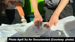 一名志愿统计受害者信息的受害者指着厚厚的一堆材料,上面记录着想要报告这起庞氏骗局的受害者信息。图片出于保护隐私的目的经过编辑。