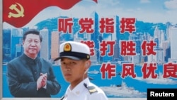 资料照：一名中国解放军海军士兵在香港的海军基地站在有着中国领导人习近平画像的宣传标语前。（2016年7月8日）