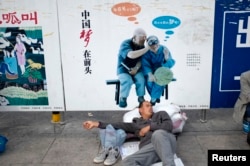 资料照:一名农民工在北京火车站的一个中国梦的政府宣传牌下打盹。