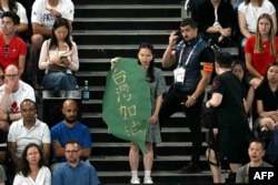 在2024巴黎奥运会羽毛球男双半决赛赛场上,一名女子手持台湾地图形状,写有“台湾加油”字样的标语,她的身后站着一名赛场警卫。(2024年8月4日)