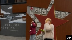 两个年轻人走过北京街头一堵政府的宣传墙。(2024年1月17日)