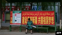 中国新疆叶尔羌地区的一名妇女坐在公交车站,车站张贴政府的宣传标语:“建设美丽新疆,共圆祖国梦想”。(2023年7月17日)