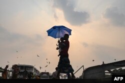 Seorang pria menggendong putranya berjalan dengan payung saat gelombang panas di Yangon pada 19 April 2023. (Foto: AFP)
