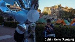 Siswa membawa balon dan mengenakan gaun untuk foto wisuda sementara siswa lainnya terus melakukan aksi protes pro- Palestina di Universitas Columbia di New York City, AS, 26 April 2024. (Foto: REUTERS/Caitlin Ochs)