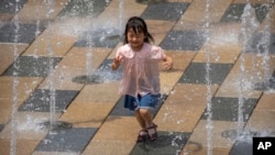 在一个酷热的夏日,一个小女孩在北京一家商场外的喷水池里嘻戏。(2022年6月25日)