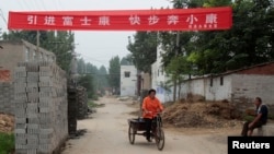 资料照:中国河南省郑州富士康工厂建筑工地旁的一个村庄,一名女子蹬着板车路过悬挂的“引进富士康,快步奔小康”的横幅标语。(2010年8月11日)