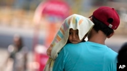 印度一名男子冒着酷暑抱着一个头上披着遮阳毛巾的幼儿走在查谟市大街上。(2024年6月2日)