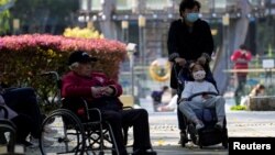 在上海一个公园里，一名女子推着小女孩路过一位坐轮椅的老人。（2023年4月2日）