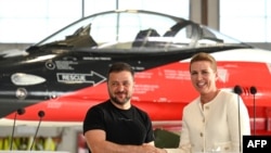 乌克兰总统泽连斯基和丹麦首相弗雷德里克森在丹麦北部沃延斯的斯克里德斯特鲁普空军基地机库的一架F-16战斗机前举行的新闻发布会上握手。(2023年8月20日)