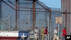资料照片:2023年5月10日,在一名美国陆军士兵的注视下,移民从墨西哥华雷斯城进入德克萨斯州埃尔帕索。