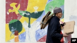 资料照:一名捡垃圾的老人拿着纸箱板从宣传中国共产党的壁画前走过。(2006年3月3日)