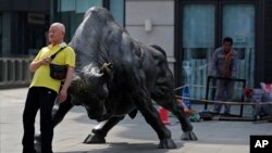 资料照:一名男子靠在北京一家证券交易所前的公牛铜像上。(2021年5月19日)