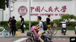 北京街头人们路过中国人民大学校园外墙的标识。(2024年7月22日)