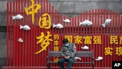 资料照:一名戴着口罩的男子在武汉街头一个中国梦的政府宣传牌下打盹。(2020年4月8日)