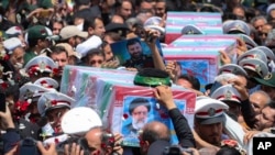 2024年5月23日,在伊朗马什哈德市举行的葬礼上,人们抬着覆盖着国旗的莱希总统及其同机人员的灵柩。(美联社照片)