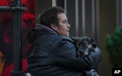 Seorang pria menutupi seekor anjing dengan jaketnya saat duduk di jalanan pada hari yang dingin, di Wina, Austria, Selasa, 23 November 2021. (AP/Vadim Ghirda)