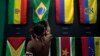 Seorang pria pribumi mengulurkan tangannya di atas bendera Brazil di paviliun delapan negara Amerika Selatan yang berbagi wilayah hutan hujan Amazon, selama pertemuan Dialog Amazon di di Belem, Brazil, 6 Agustus 2023. (Foto: AP)