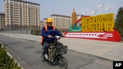 中国河北雄安街头一名工人骑车路过一处口号宣传牌。(2023年4月1日)