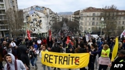 抗议民众在法国南部马赛市沿圣查尔斯火车站拾级而上,队伍前面的黄色横幅上的法文“RETRAITE”意思是“退休”,但是该法文词中最后一个字母“E”被打上红X,去掉了“E”这个词的意思就变成”取消“或”去除“。法国民众用讽刺的方法对马克龙政府的延迟退休计划表达反对和抗议。