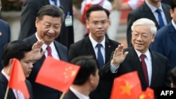 资料照片:2017年11月12日,在河内举行的欢迎仪式上,中国国家主席习近平(左)和越南共产党总书记阮富仲(右)向举着越南和中国国旗的学生挥手致意。(法新社照片)