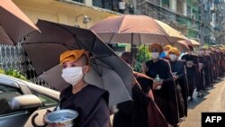 Para biarawati Buddha mengumpulkan sedekah dengan kepala ditutupi handuk dan payung untuk berlindung dari sinar matahari saat gelombang panas melanda Yangon pada 24 April 2023. (Foto: AFP)