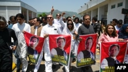 资料照片:巴基斯坦正义运动党 (PTI) 议员在伊斯兰堡议会大厦外举行抗议活动时举着印有被监禁的前总理伊姆兰·汗照片的标语。(2024年7月18日)