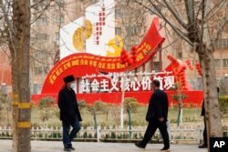 资料照:新疆和田居民走过街头竖立的社会主义核心价值观的宣传牌。(2021年3月22日)