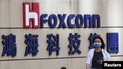 资料照:一名女子走过台北鸿海科技集团大楼外的富士康标识。(2922年11月9日)