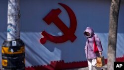 一名女子走过北京一处住宅小区围墙上的中共标识。(2024年3月1日)