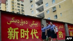 资料照:三位姑娘走过新疆莎车县街头的一幅宣传标语。(2023年7月18日)