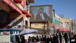 资料照:新疆居民排队进入和田一家大市场之前接受哨卡检查,旁边的大屏幕正在播放中共领导人习近平的新闻。(2017年11月3日)