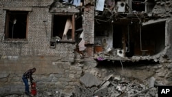 10月14日,在乌克兰东部康斯坦丁诺夫卡,一名居民正在清理遭到俄罗斯连夜炮击的房屋残骸。