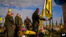 乌克兰军人在“保卫者日”这天在哈尔科夫一座最近阵亡的战友墓地前放置鲜花,寄托哀思。(2022年10月14日)