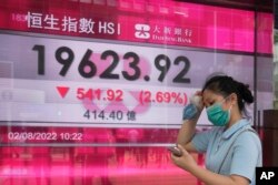 周二香港街头,一名女子走过恒生指数显示大跌的电子显示牌。(2022年8月2日)