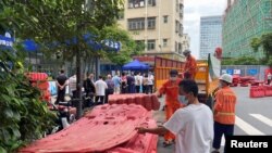 中国广东深圳的工人正在准备给一住宅小区外竖立围栏,与此同时小区居民正在排队做核酸。(2022年8月29日)