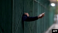 一名居民从北京潘家园一个封控小区的栅栏里伸出握着手机的手。(2022年4月27日)