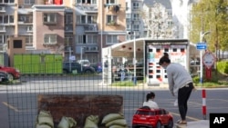 3月29日,上海一座被封闭小区内一位妈妈正陪着女儿玩玩具。她们身旁不远处是用铁丝网,三合板及沙袋构筑的临时封闭路障。