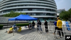 资料照片:人们在北京一个办公楼区排队等候进行新冠病毒核酸检测(2022年4月29日)