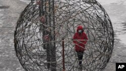 一位身着红衣戴着口罩的北京妇女正走过一个球形的编制艺术作品。中国实行的新冠病毒”清零“政策名为保护人民和经济,但实际效果可能会使中国更难摆脱疫情的肆虐。(2022年1月22日)