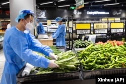 中共官媒新华社发布照片显示身穿防护服的人员在上海徐汇区超市里出售蔬菜。(2022年5月16日)