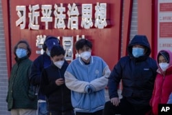 北京市民在宣传习近平思想的标语墙前排队等候进行核算检测。(2022年12月5日)