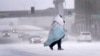 A person wrapped in a blanket crosses a snow-covered street, Dec. 22, 2022, in St. Louis. Snow and frigid temperatures have moved across the U.S., complicating holiday travel and plans in the coming days.