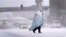 A person wrapped in a blanket crosses a snow-covered street, Dec. 22, 2022, in St. Louis. Snow and frigid temperatures have moved across the U.S., complicating holiday travel and plans in the coming days.