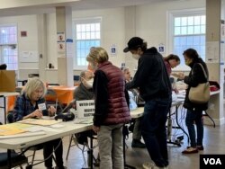Pemilih menunjukkan kartu identitas untuk mendapatkan surat suara dan memberikan suara di kotak suara di TPS di masjid komunitas Indonesia: IMAAM Center di Silver Spring, Maryland.